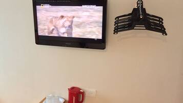 Un televisor montado en la pared mostrando un programa, una tetera roja y una bandeja blanca sobre una mesa.
