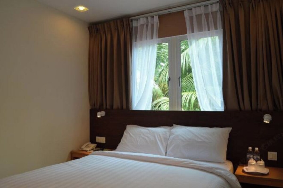 A hotel room with a bed, a nightstand, a telephone, and a window with curtains.