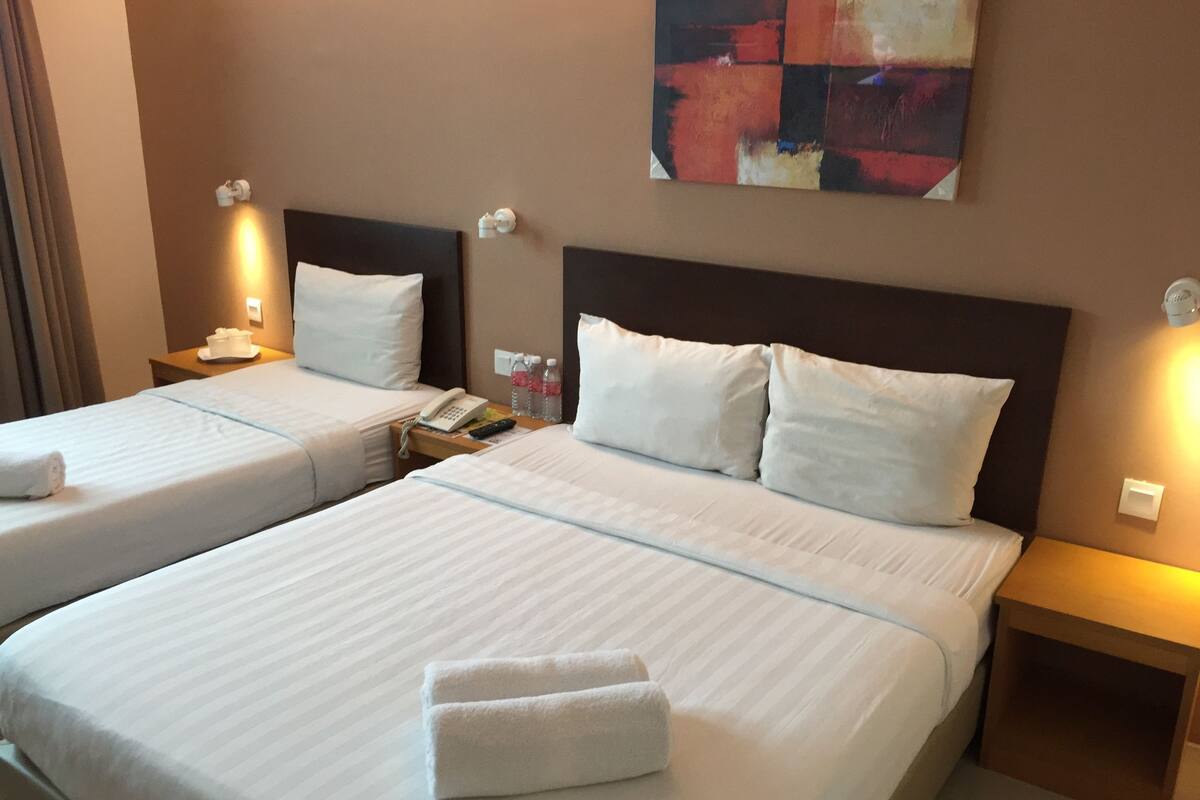 Two single beds with white linens, a bedside table with a phone and remote control, and a painting on the wall.
