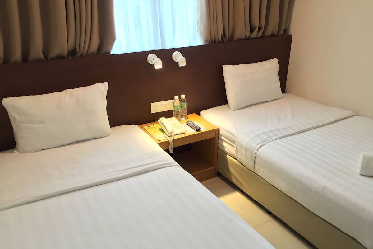 A hotel room with two single beds, a wooden nightstand with a phone, remote controls, and a bottle of water.