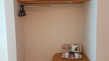 A compact workspace with a flat-screen TV mounted above a wooden desk, a chair, and a small table with a kettle and cups.