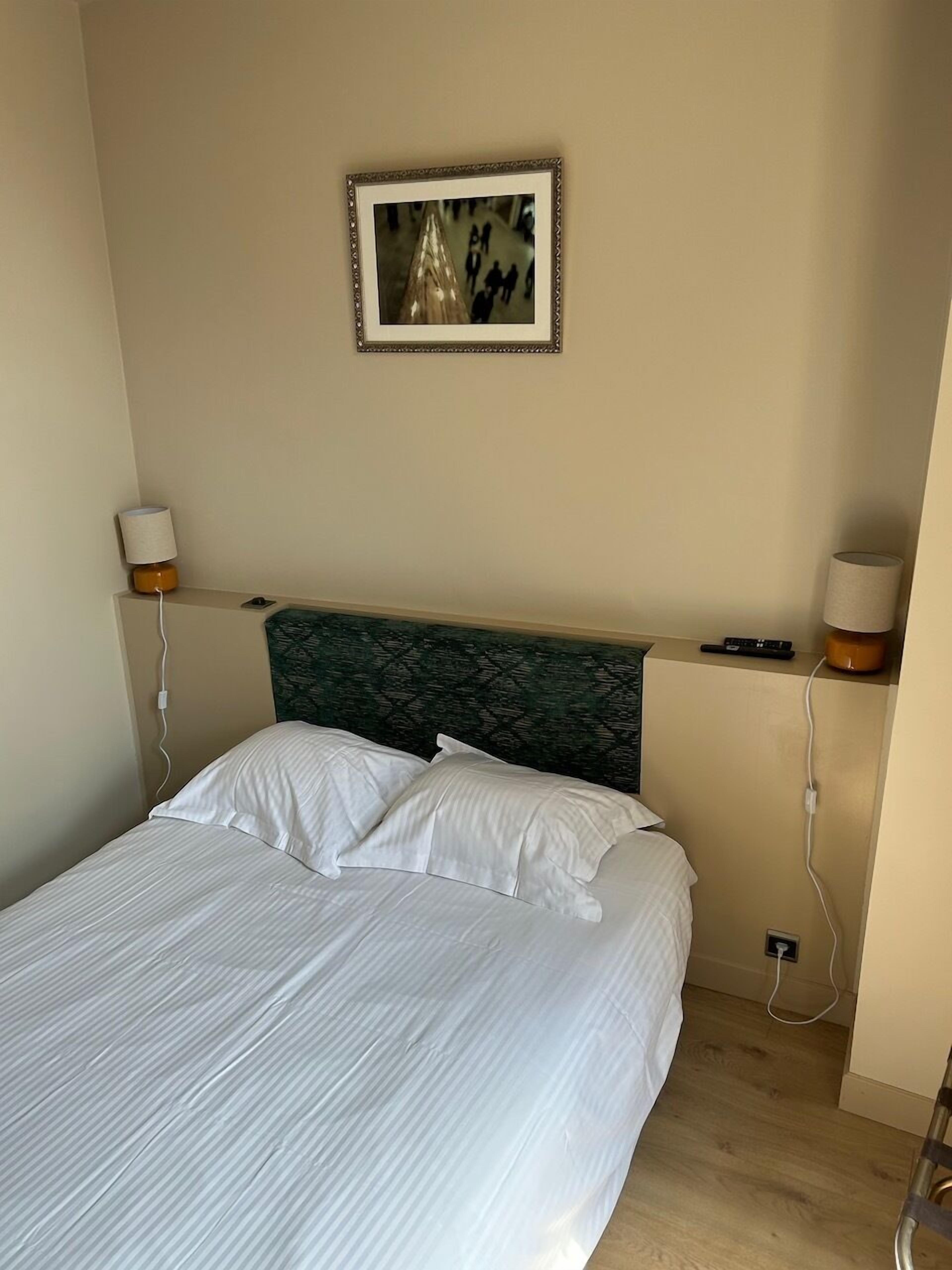 Una cama bien hecha con sábanas blancas, un cabecero verde y dos lámparas de noche.