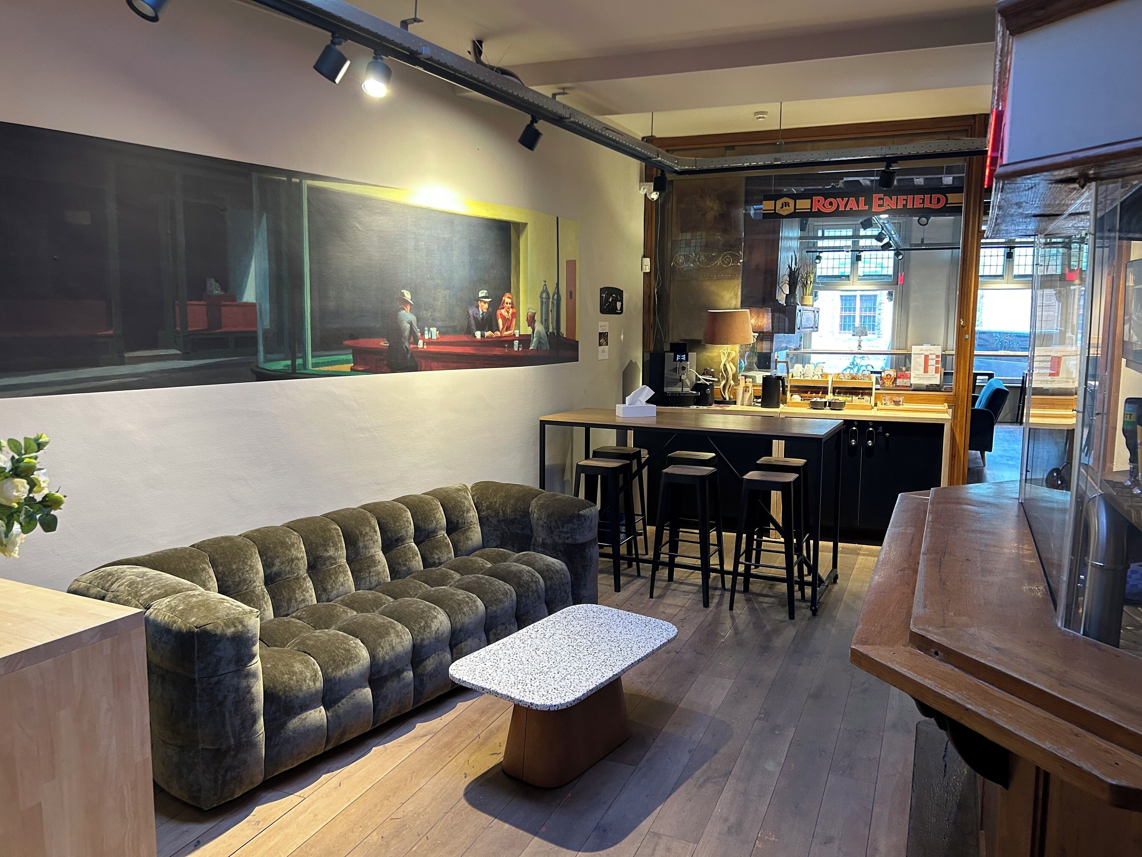 A modern interior with a sofa, bar stools, a coffee machine, and a painting on the wall.