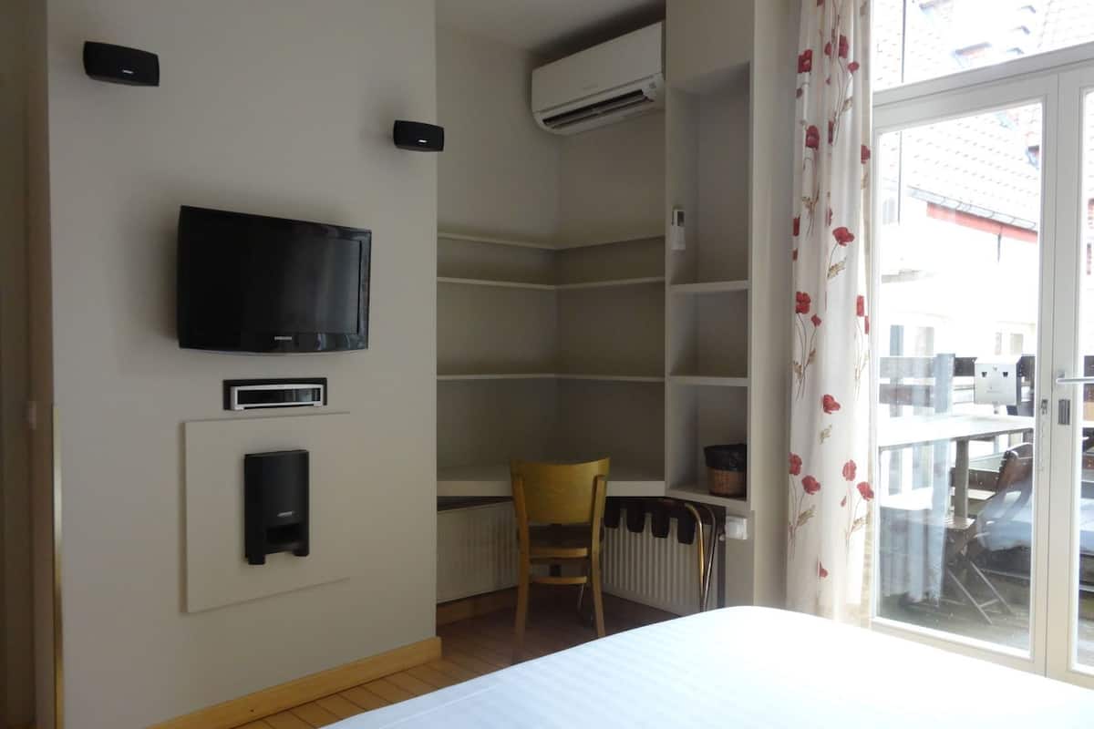 Quarto de hotel com uma cama, televisão, radiador, cadeira e janela com vista para o exterior.
