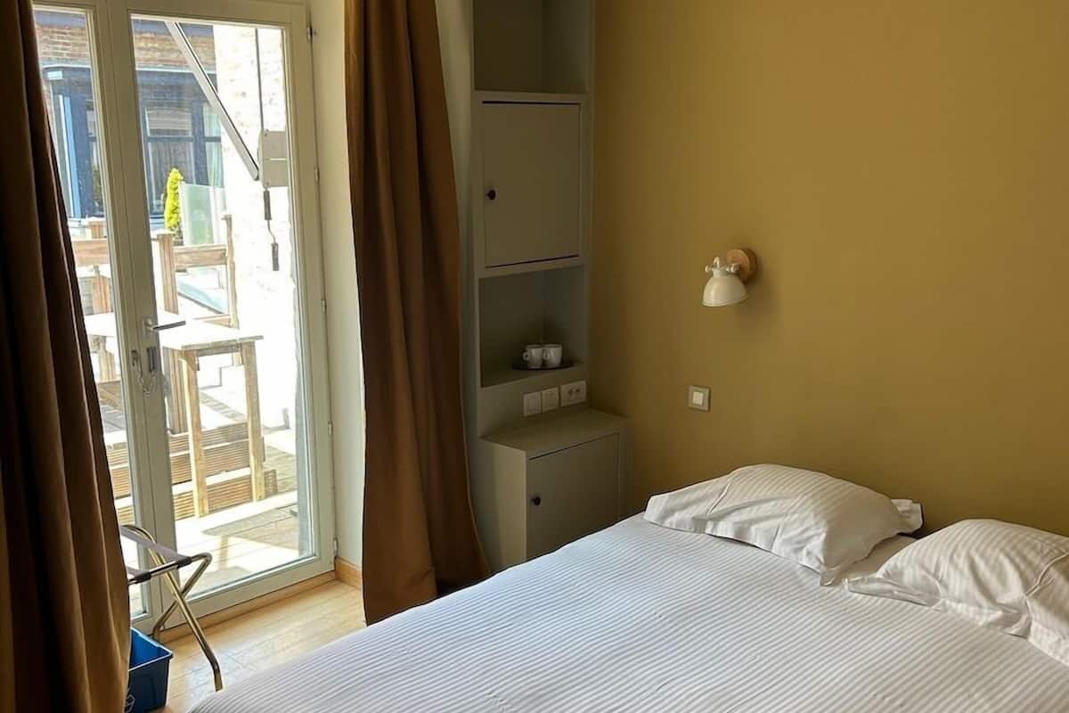 Quarto de hotel com cama, mesa de cabeceira pequena, guarda-roupa e vista para o exterior.