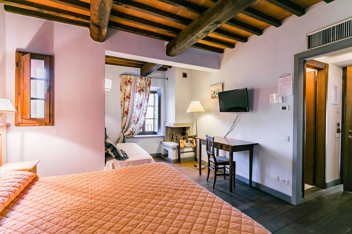 Een slaapkamer met een bed, een bureau, een stoel, een televisie en een raam met gordijnen.