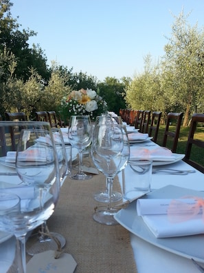 A long table set outdoors with wine glasses, plates, and napkins, surrounded by trees. - Le Fonti a San Giorgio (Montespertoli)