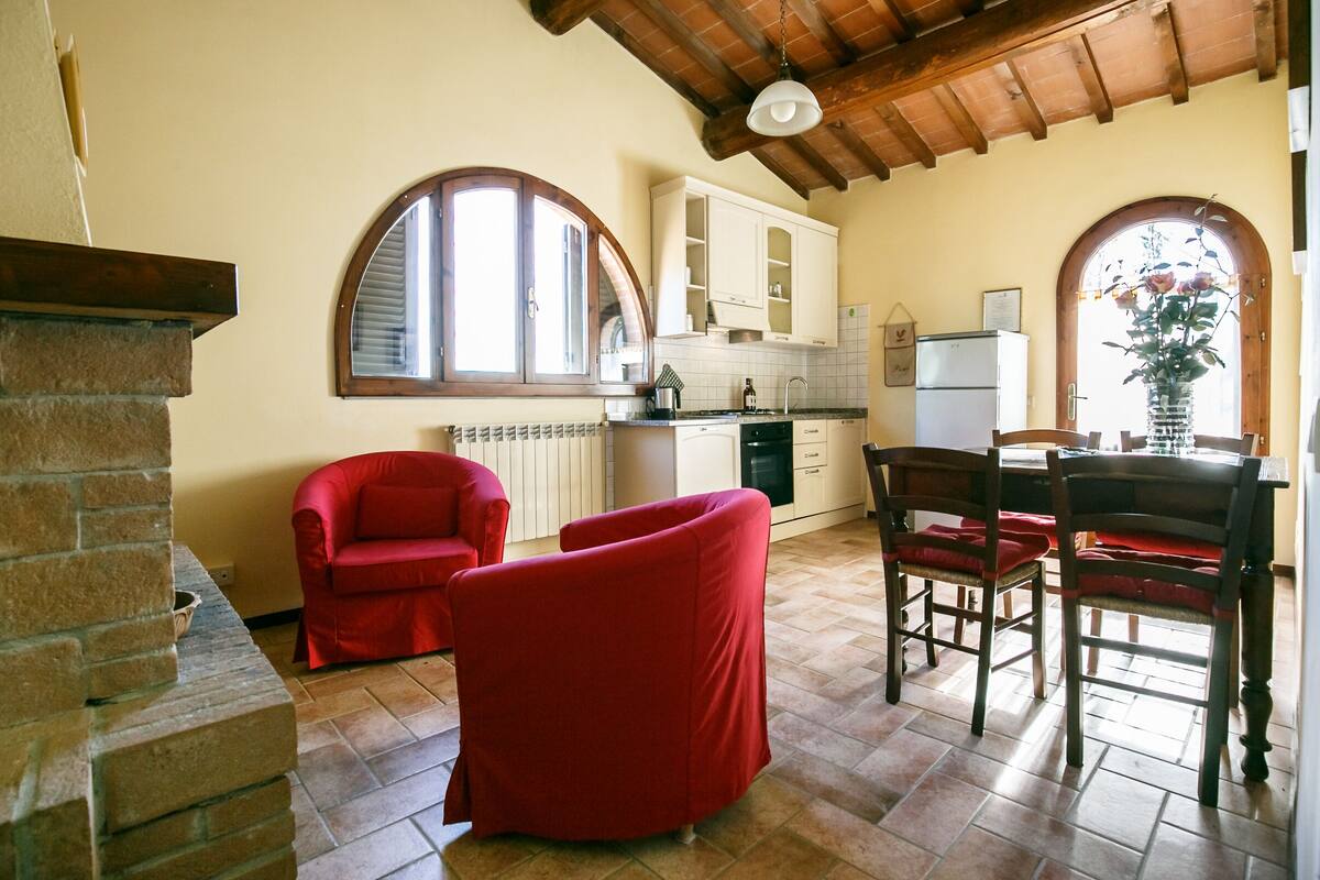 Een keuken met een stenen open haard, rode stoelen en een eettafel met stoelen.