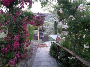 A garden pathway leading to outdoor seating with a pergola and a view of a hilly landscape.