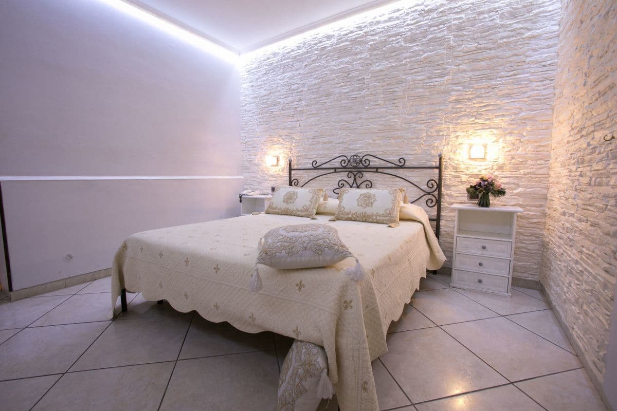 Un dormitorio con cama, mesitas de noche y pared de piedra.