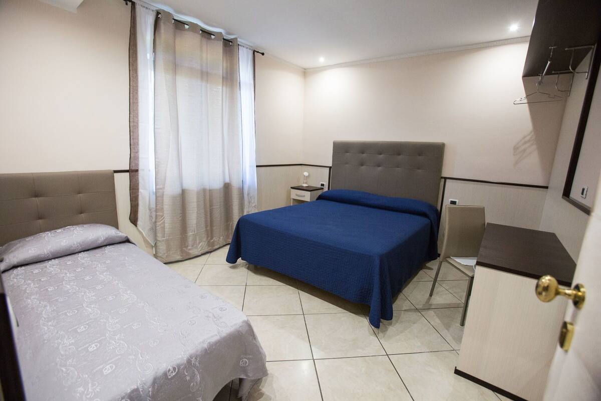 Habitación de hotel con dos camas, una mesita de noche, un escritorio, una silla, un armario y la puerta del baño.