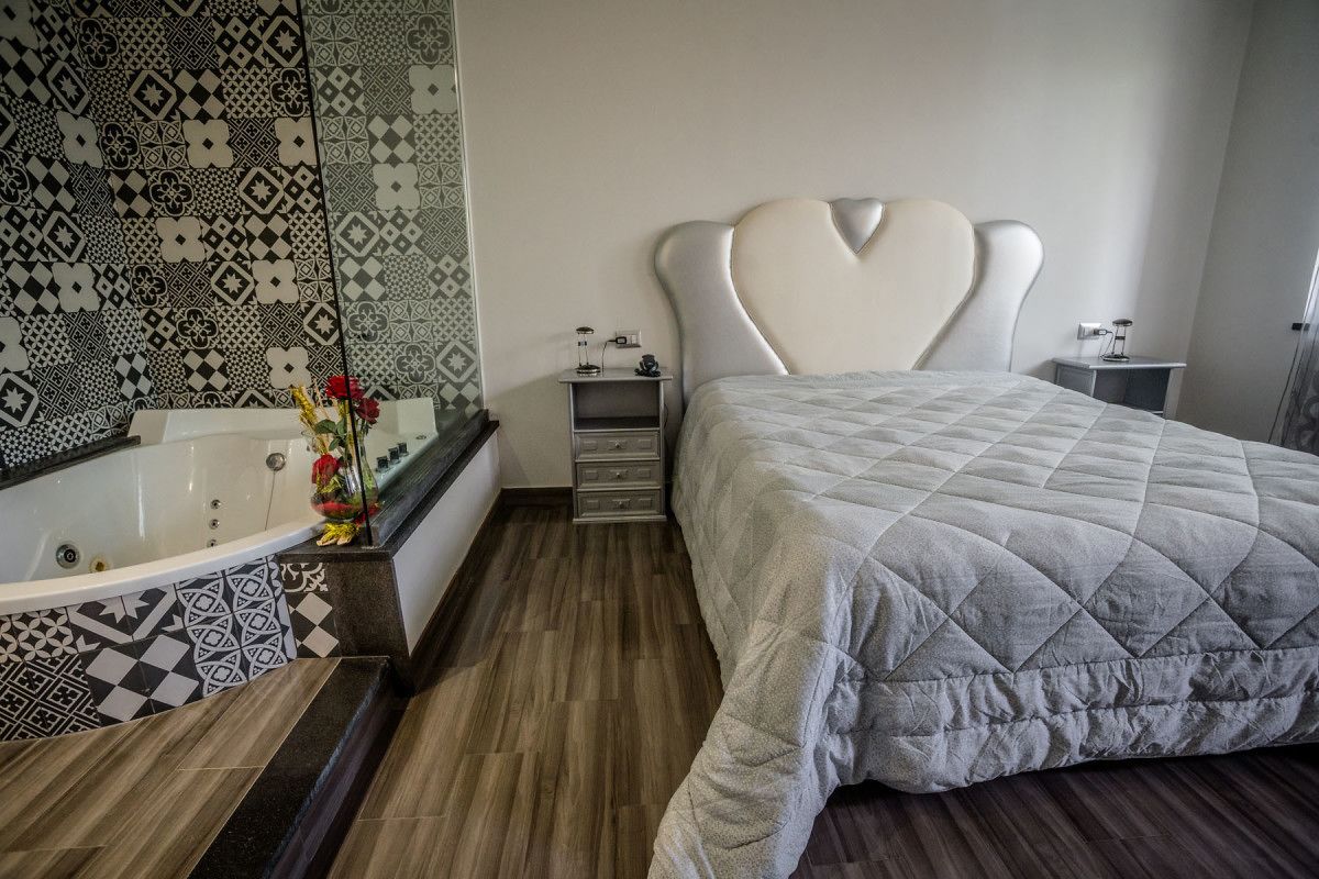 Ein modernes Schlafzimmer mit einem großen Bett, einem herzförmigen Kopfteil, einer Badewanne und Wandverkleidung mit Muster.