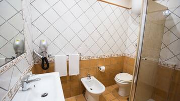 Een badkamer met een wastafel, bidet, toilet en een douchecabine met glazen wanden.