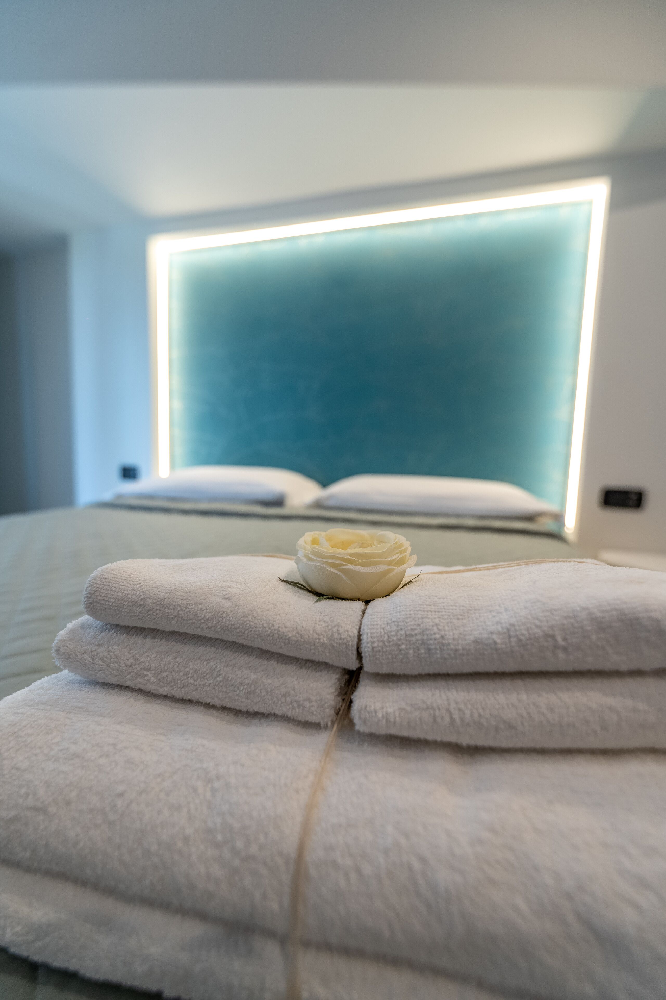 Una cama bien hecha con toallas blancas dobladas y una sola rosa blanca.