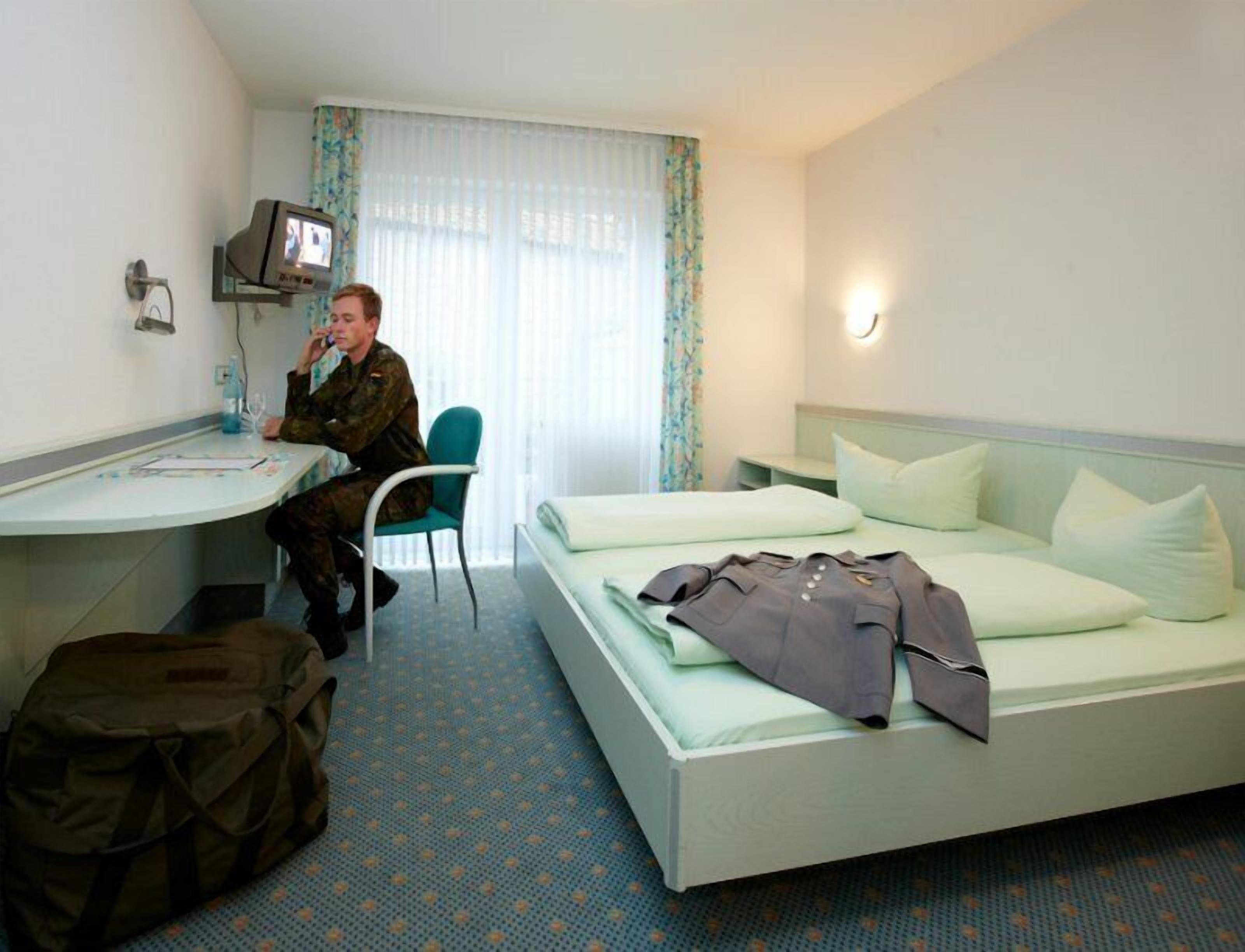 Habitación de hotel con cama, escritorio, silla, televisor y ventana con cortinas.
