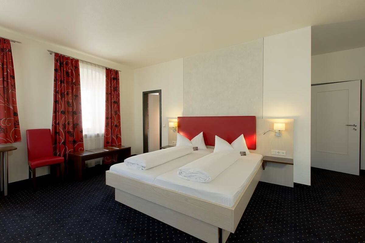 A hotel room with a large bed, two bedside tables, a desk, a chair, and a wardrobe.