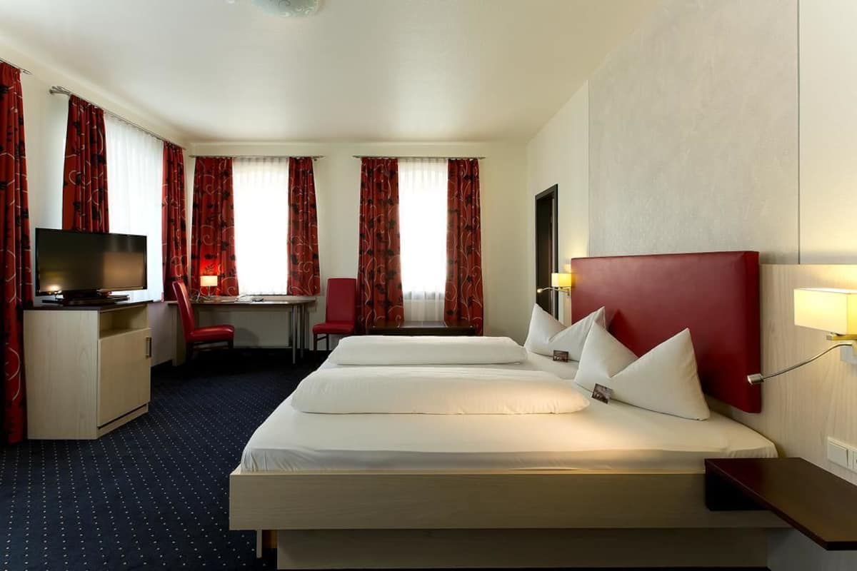 A hotel room with two beds, a desk, a TV, and a chair.