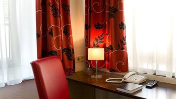 A hotel room with a desk, a telephone, a remote control, and a lamp.