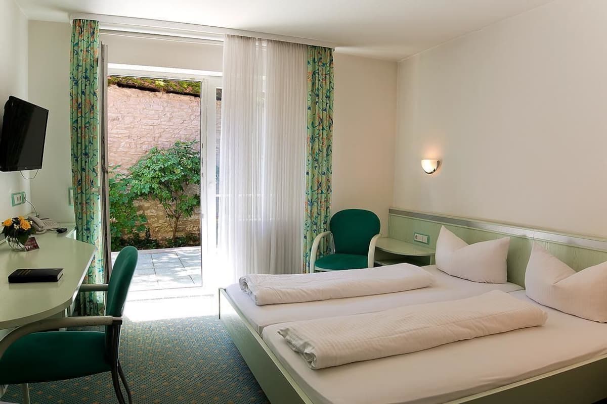 A hotel room with a bed, a desk, a chair, a television, and a window with curtains.