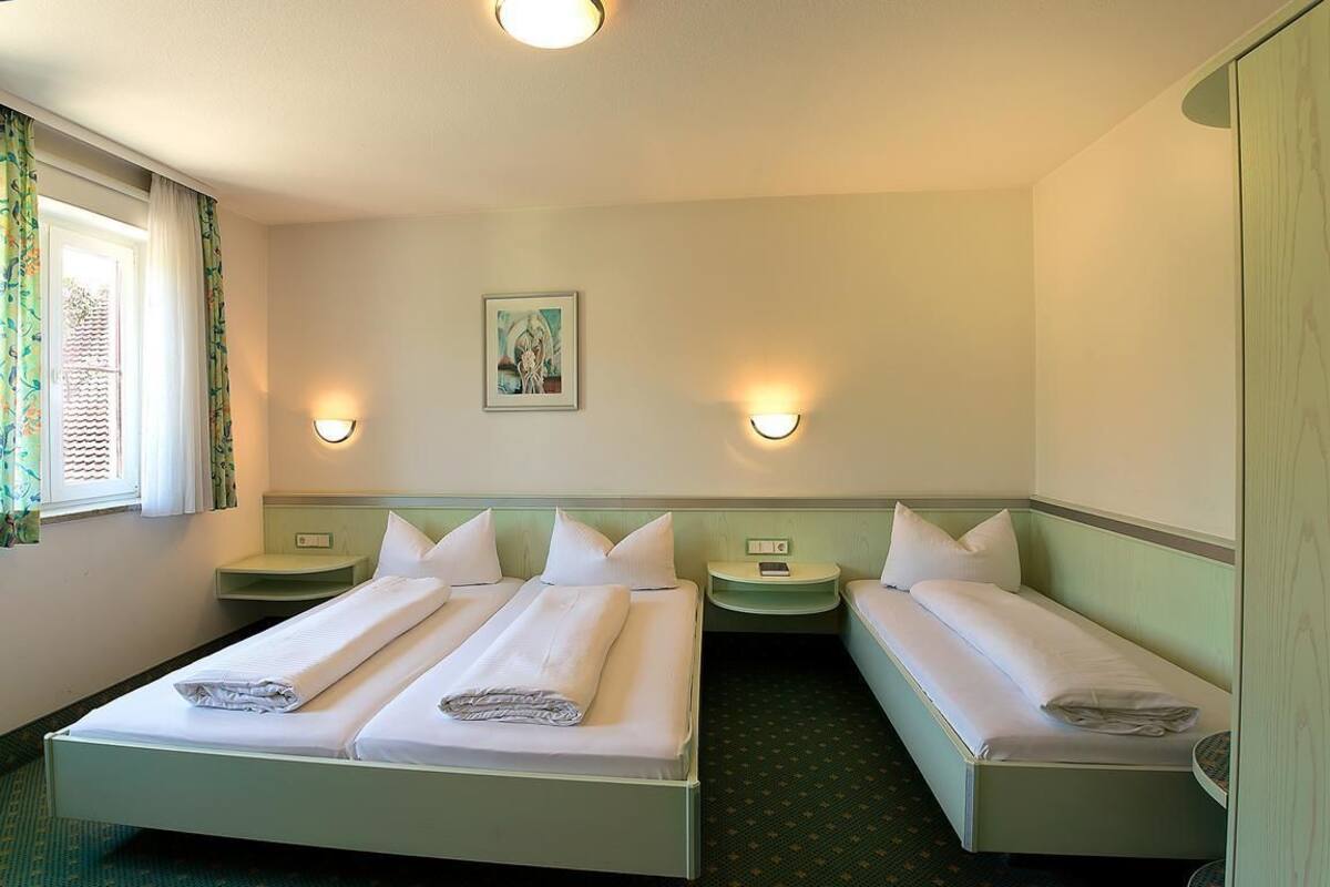 A hotel room with two beds, a window with curtains, and two wall-mounted lamps.
