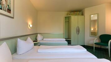 A hotel room with two beds, a green chair, a wardrobe, and a painting on the wall.