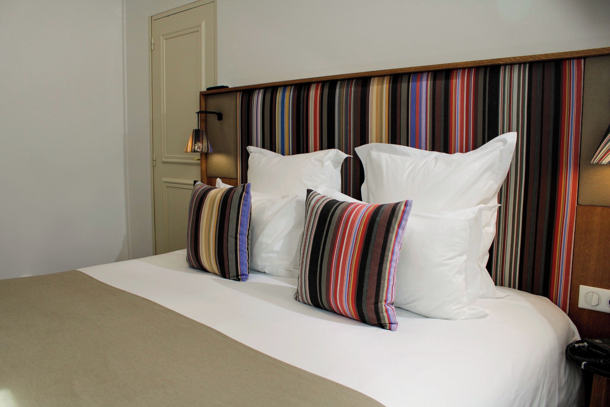 Una habitación de hotel con una cama, almohadones a rayas, un cabecero y una puerta.