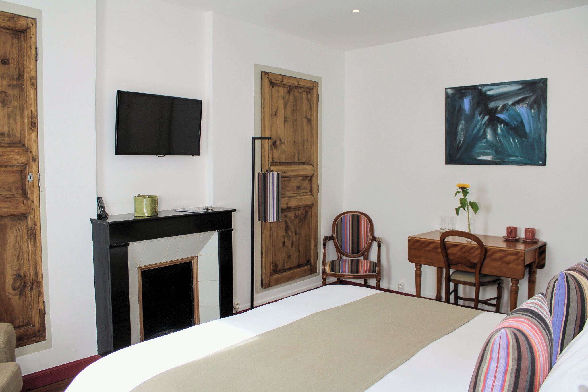 Une chambre à coucher comprenant un lit, une télévision, une cheminée, une table à manger avec des chaises et un tableau au mur.