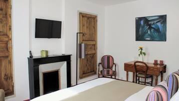 Une chambre à coucher comprenant un lit, une télévision, une cheminée, une table à manger avec des chaises et un tableau au mur.