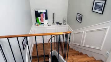 Una escalera con barandilla de madera y balaustradas negras, que conduce a un rellano con una mesa consola blanca.