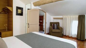 Un dormitorio con cama, una silla, un armario y una puerta que da a un baño.