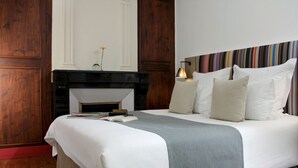 Una cama bien hecha con un cubrelecho gris, una lámpara de noche y un libro en la mesita.