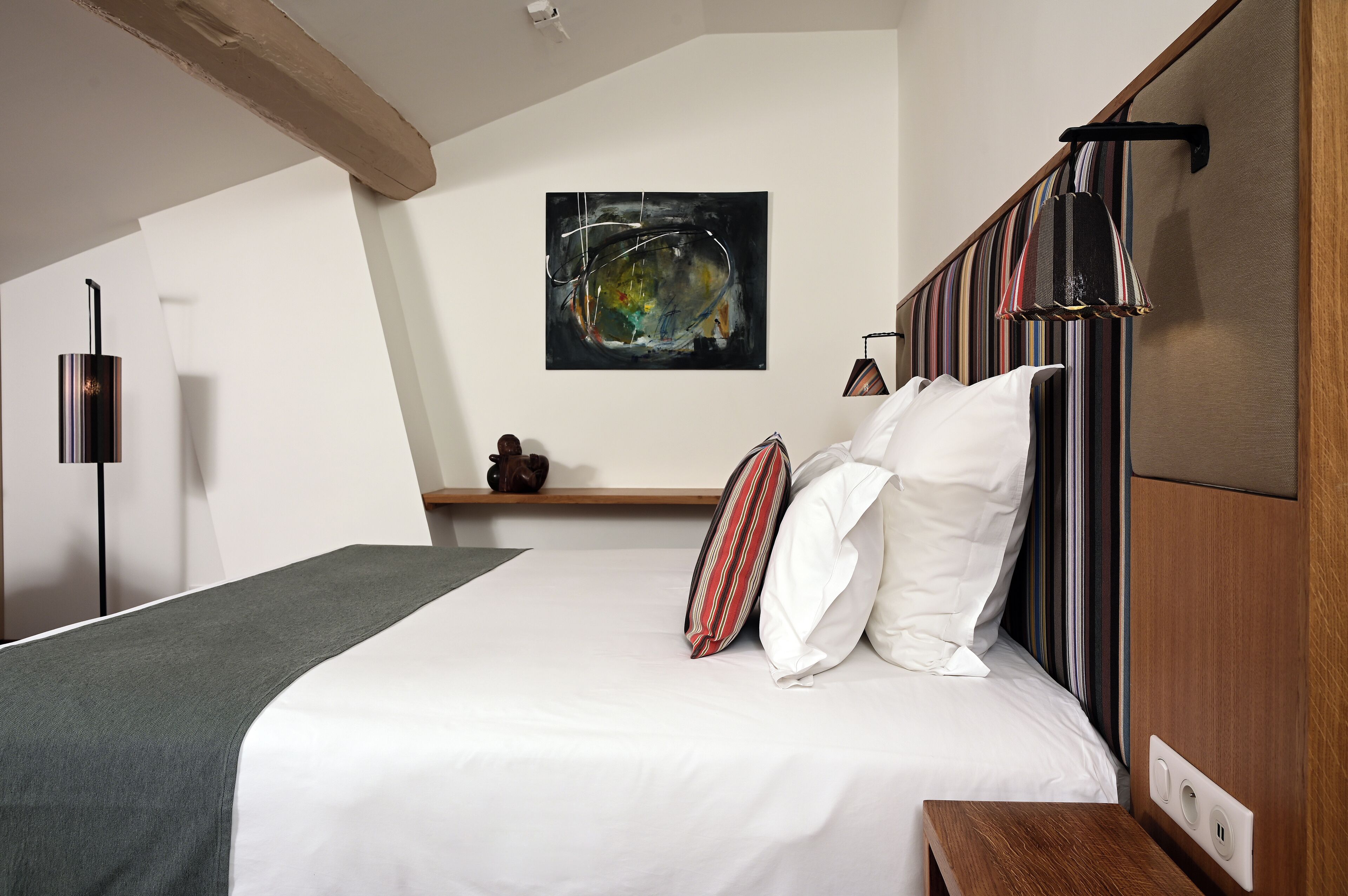 Una habitación de hotel moderna con una cama grande, cabecera de madera, una obra de arte colgada en la pared y una mesita de noche.