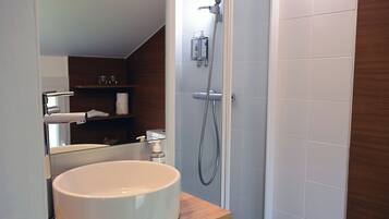 A bathroom with a white sink, a mirror, a shower, and a wooden shelf with toiletries.