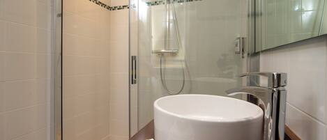 A modern bathroom with a glass-enclosed shower, a large white sink, and a mirror above it.