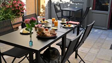 Una mesa con desayuno servido, un jarrón con flores y un gato debajo de la mesa.