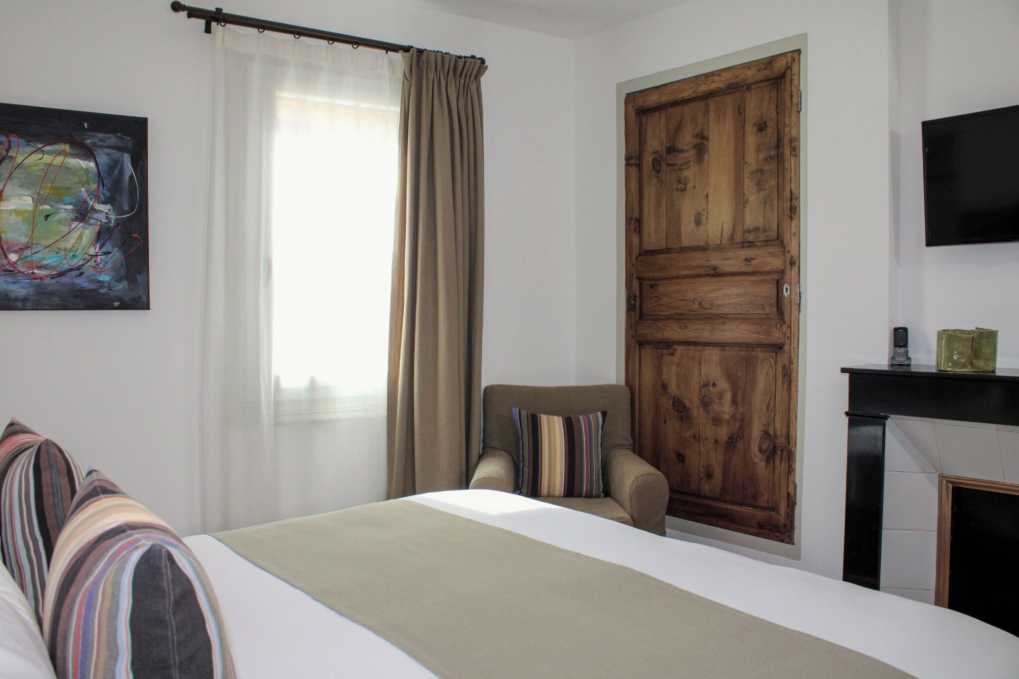 Een hotelkamer met een bed, een stoel, een houten deur, een schilderij en een televisie.