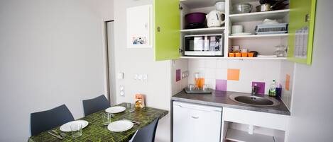 A compact kitchen with a dining table, chairs, a microwave, a sink, and a small refrigerator.