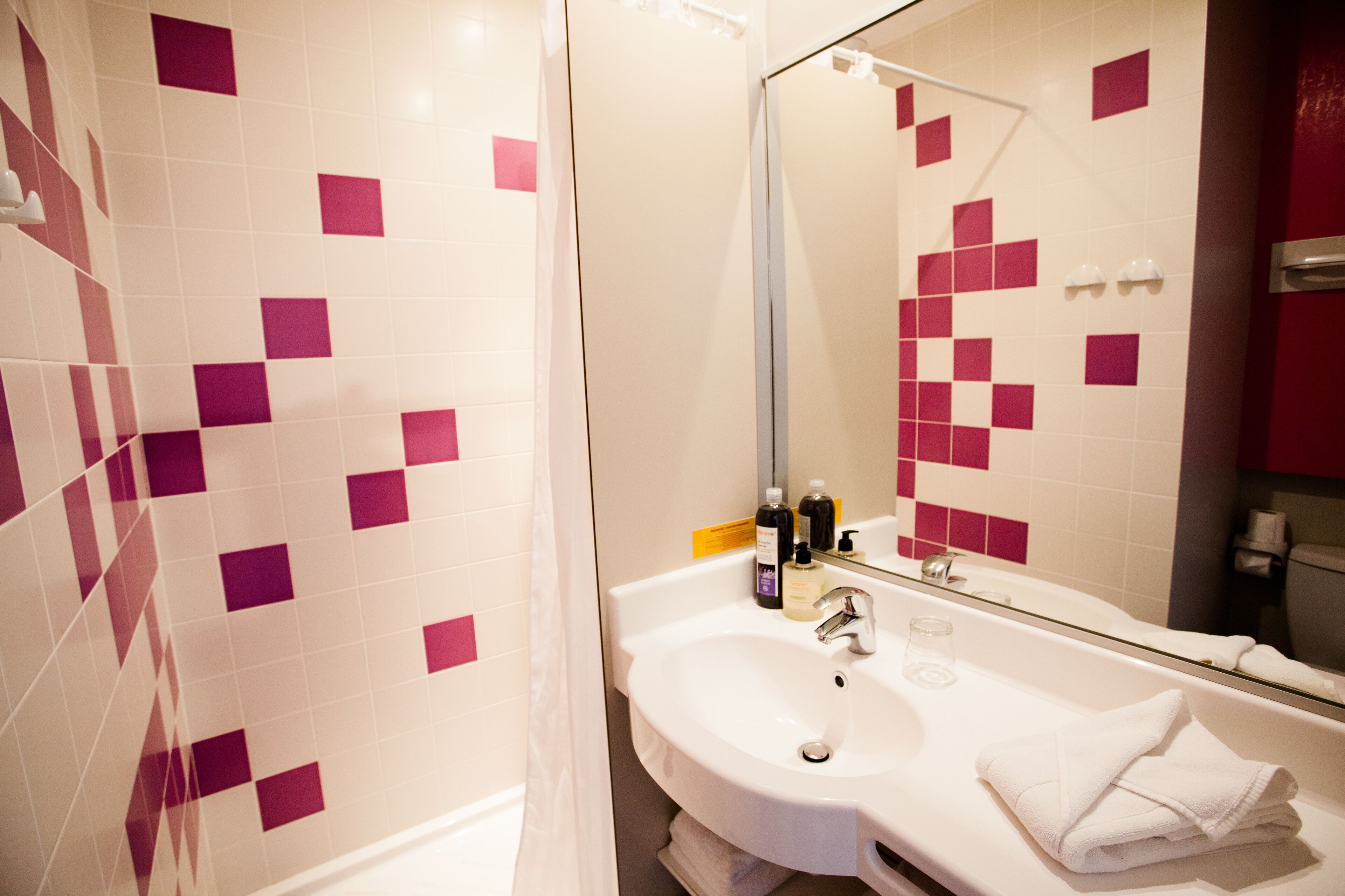 Een badkamer met een witte wastafel, een glazen douchecabine en een spiegel die het interieur van de badkamer weerspiegelt.