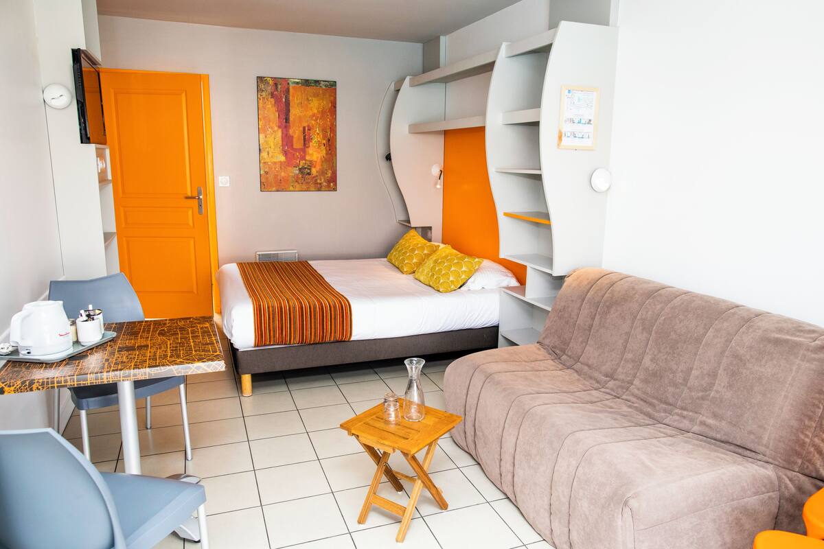 Ein Hotelzimmer mit einem Bett, einem Schlafsofa, einem kleinen Tisch mit einer Kaffeemaschine und einem an der Wand befestigten Regal.