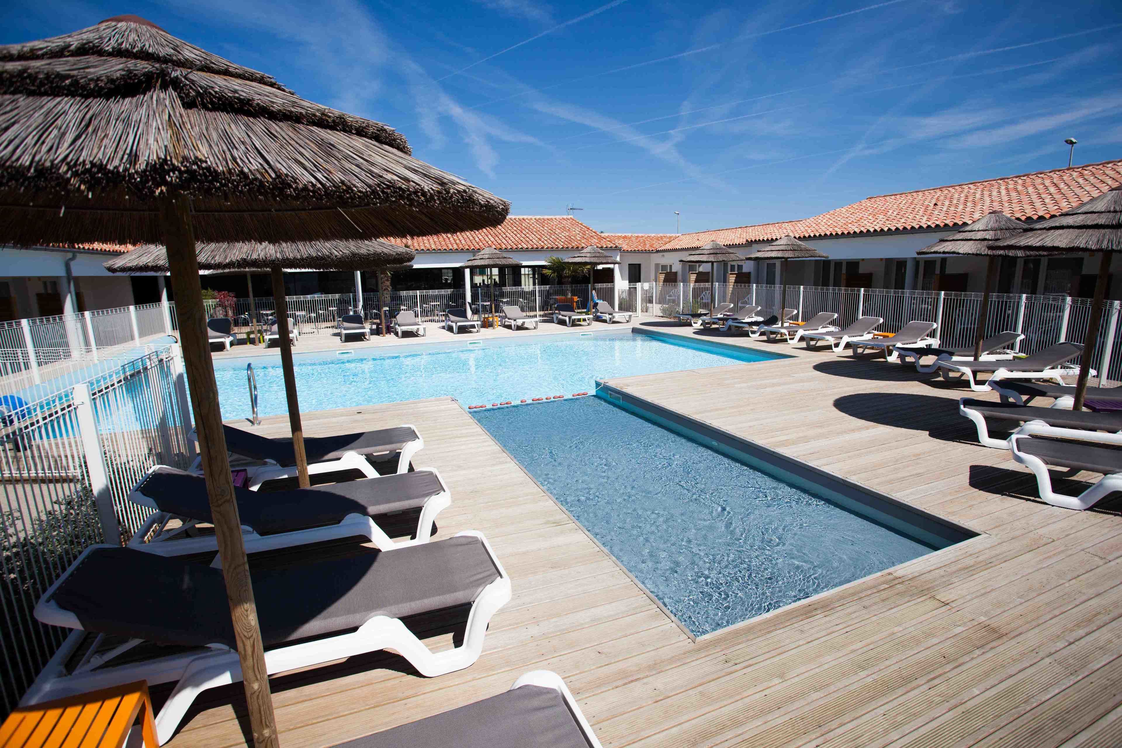Un espace aménagé au bord de la piscine, avec des chaises longues, des parasols et une piscine.