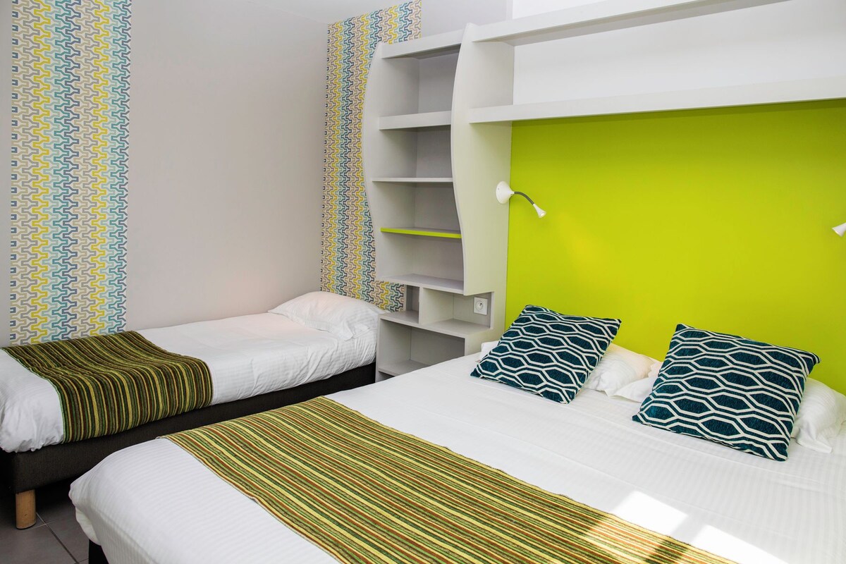 A room with two beds, a green accent wall, and patterned wallpaper.