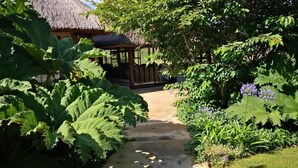 A garden pathway leading to a wooden structure with a thatched roof. - Amazian Mountain River Lodge (Underberg)