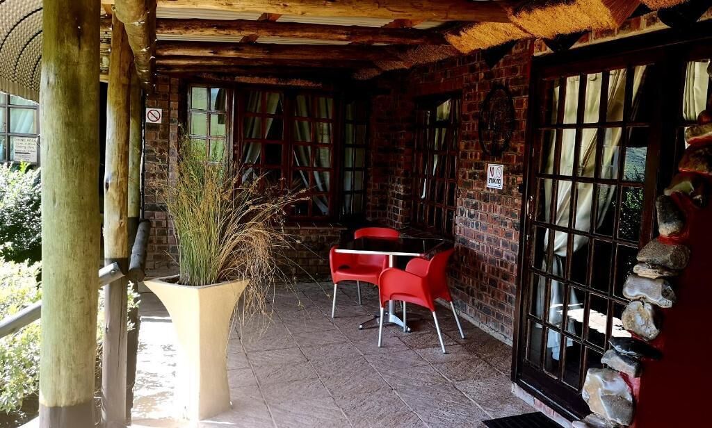 An outdoor patio with a brick wall, a large potted plant, and red chairs.