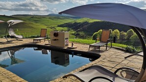 A pool area with lounge chairs and umbrellas, surrounded by a scenic view of rolling hills. - Amazian Mountain River Lodge (Underberg)