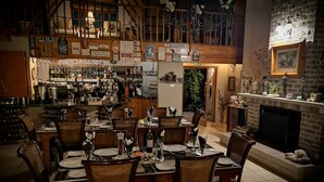 A cozy restaurant with a high ceiling, wooden beams, and a variety of wine bottles and glasses displayed on shelves. - Amazian Mountain River Lodge (Underberg)