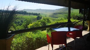 A terrace with a table and chairs overlooking a green valley. - Amazian Mountain River Lodge (Underberg)