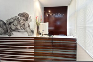 A reception desk with a modern design, a computer, and a vase with flowers. - Navona Suites (Rome)