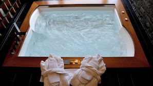 A large bathtub with a wooden frame, a control panel, and two towels on the floor.