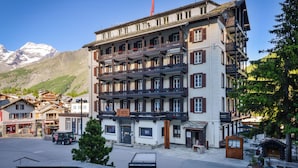 A multi-story hotel with balconies, a mountain backdrop, and a clear sky.