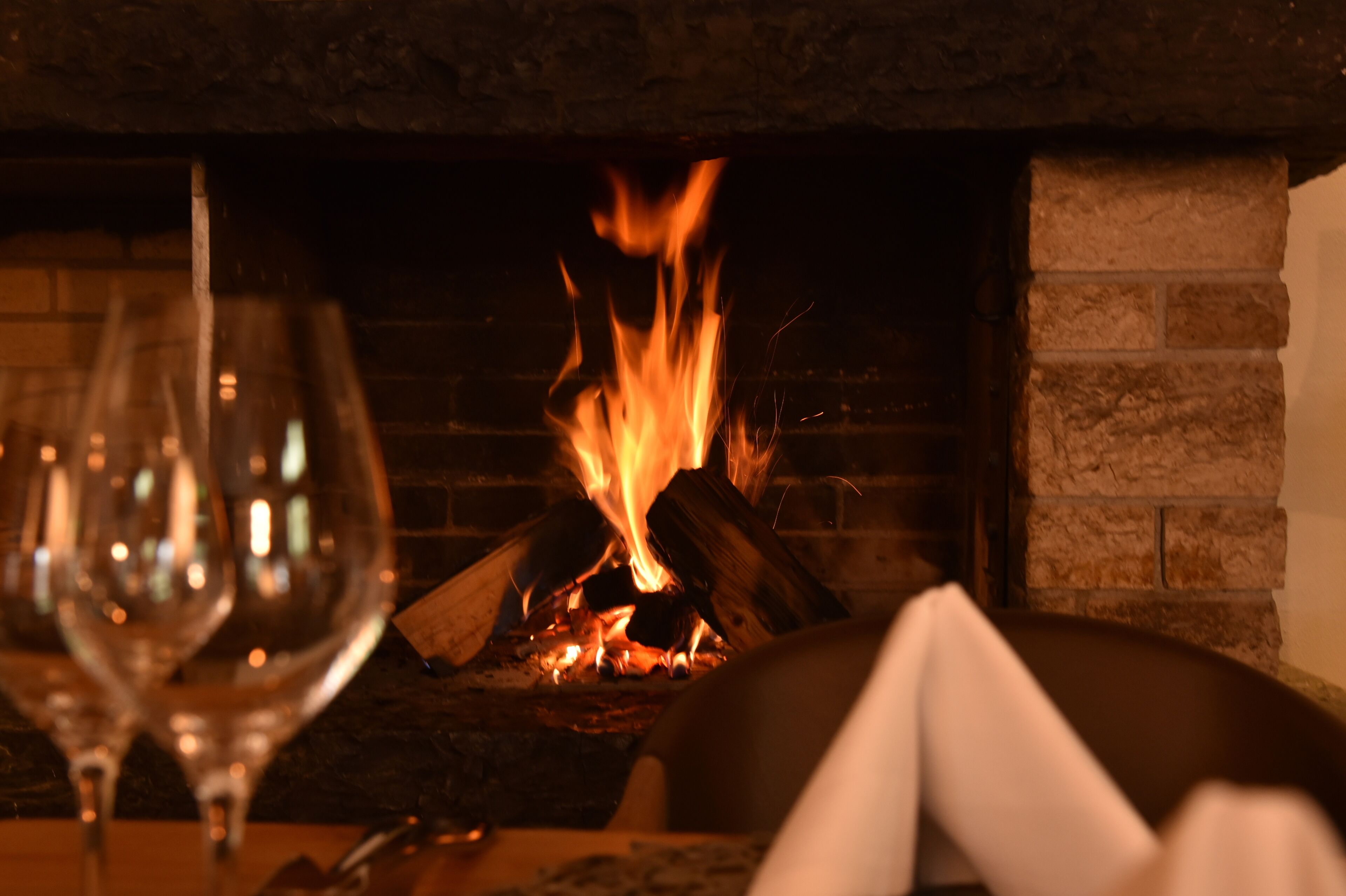 A fireplace with visible flames, a glass of wine, and a napkin on a table.